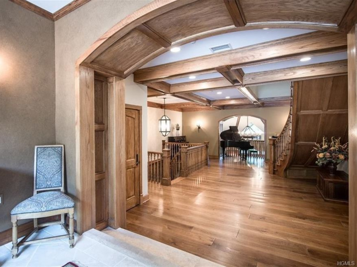The grand entryway features wooden archways, a winding staircase, and a piano.