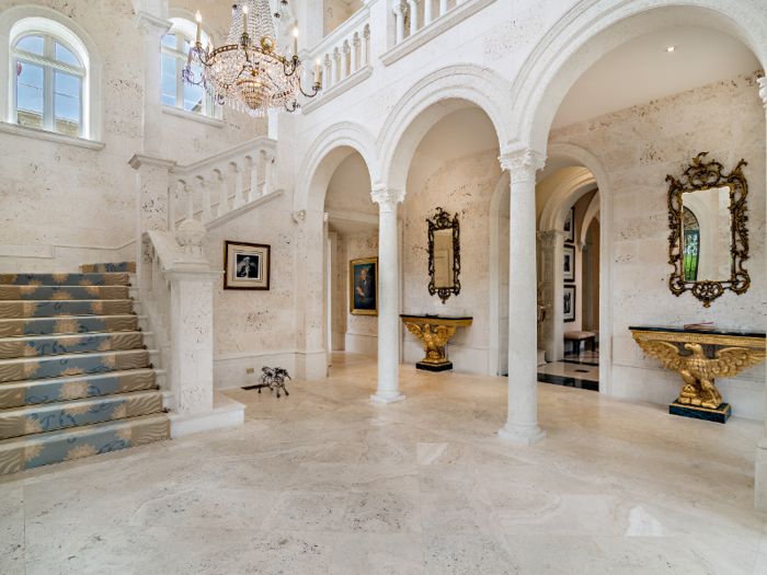 The limestone entrance foyer features 25-foot tall ceilings, a chandelier, and decorative archways.