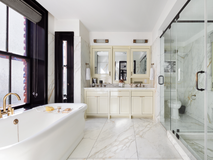 In the luxurious master bathroom is a standalone deep soaking tub, a glass-walled shower, and Calacatta Gold marble slabs on the floor and walls.