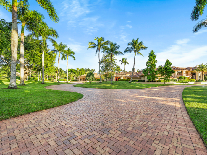 ... and a massive main driveway. The property also features palm trees and carefully groomed flower beds.