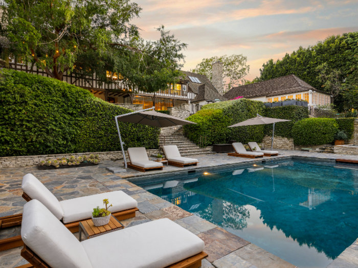 The pool area includes shaded lounge chairs and privacy hedges.