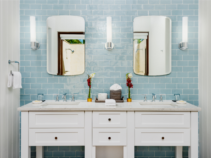 Though all bathrooms include frameless mirrors and modern light fixtures, each differs slightly. One bathroom is decorated with blue, brick-patterned tiles ...