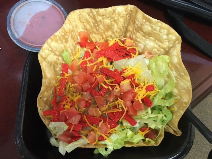 The Fiesta Taco Salad — without meat — is a hearty option that comes with salsa, tomatoes, beans, seasoned rice, lettuce, and, for non-vegans, cheese and sour cream. There are also crunchy red strips of tortillas. However, Taco Bell notes that the shell is not considered AVA-certified because it