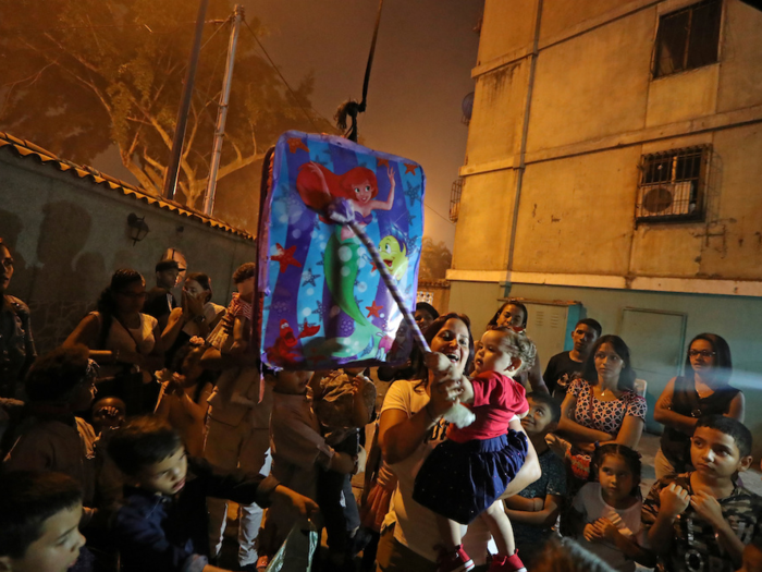 A woman holds a child as they get ready to hit a piñata.