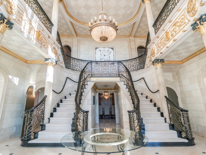 Inside the mansion, the foyer is flanked by a double staircase. With marble pillars, gold gilding, and a crystal chandelier, the entryway nods to its roaring twenties origins.