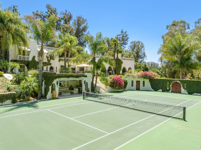 A private tennis court sits in front of the house. The property also features a swimming pool.