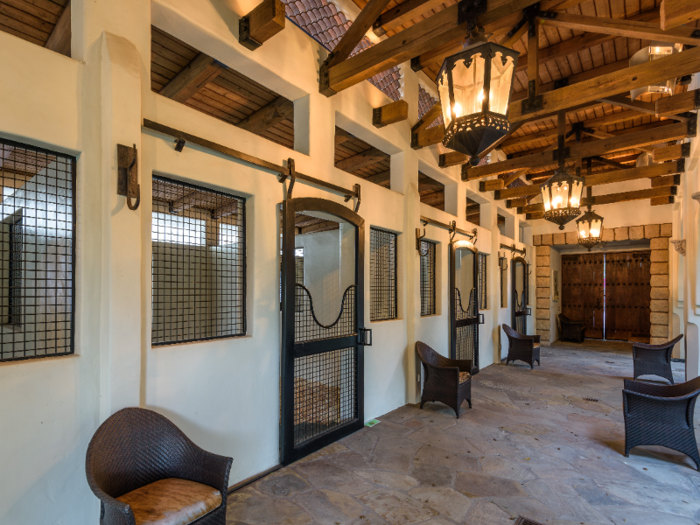 Inside, the open-air stables reveal five stalls and seating for visitors. The interior is painted white with dark wood accents.