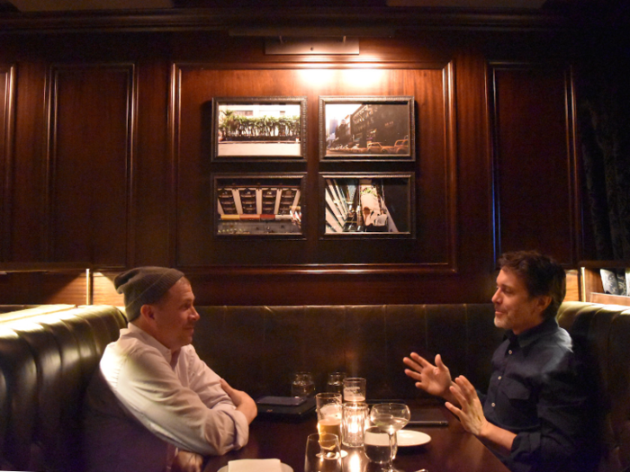 The lively, stand-up bar area is surrounded by leather booths where guests can order food. Above them are what looks to be New York City-inspired photography.