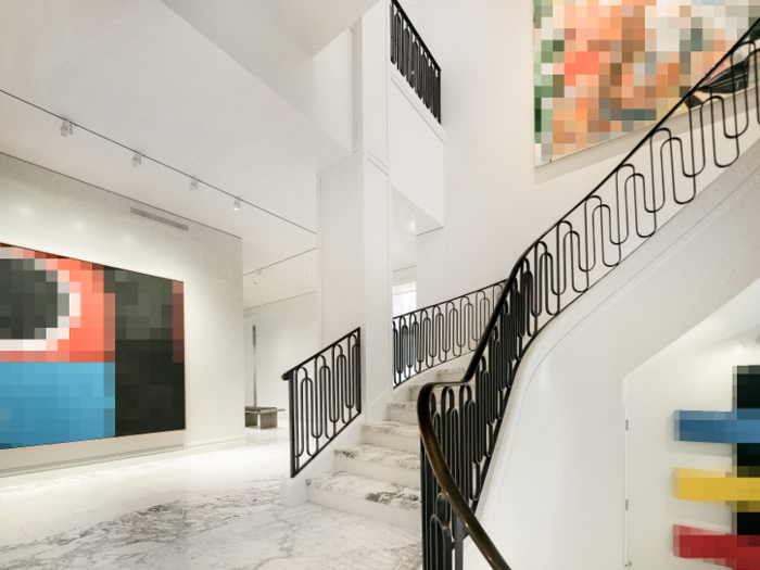 A white Carrara marble staircase with wrought-iron railings spirals up from the main level to the second floor.