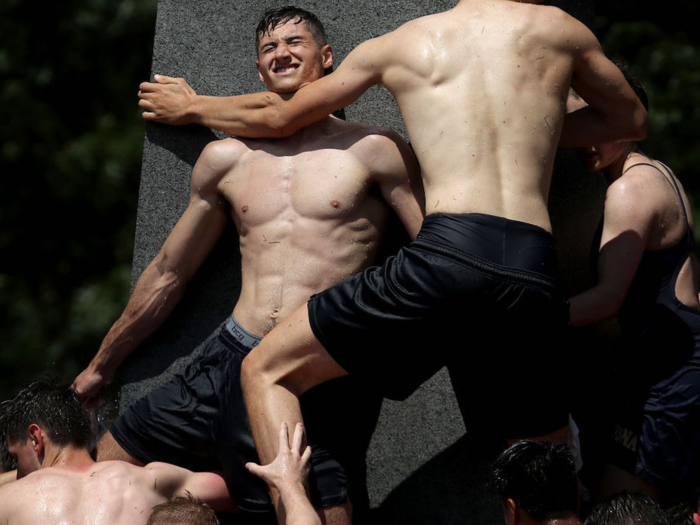 The monument is greased with as much as 50 pounds of vegetable shortening. To get a grip, the plebes climb up on the shoulders of their classmates and hold on as long as they can as others step onto their shoulders.