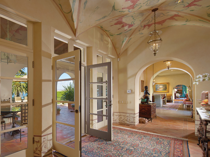 Inside, French doors open to reveal spacious hallways with painted ceilings.