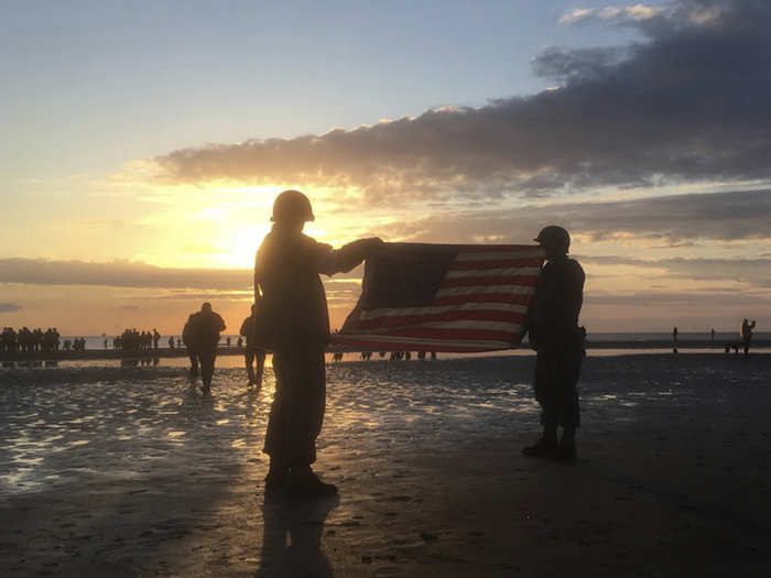 Here, two re-enactors carried a US flag to remember the American soldiers who took part in the landings.