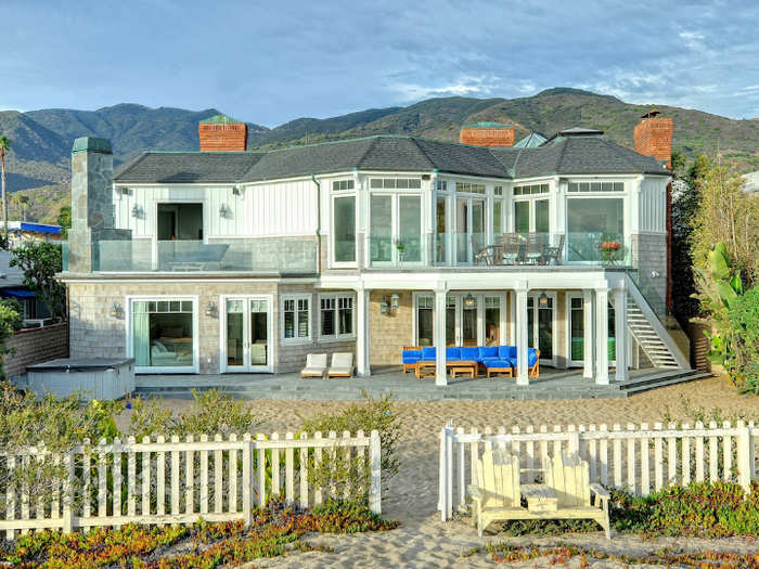 The back of the house features access to a private beach, outdoor seating, and a hot tub.