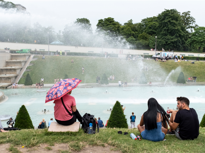 Some people are taking cover from the sun with umbrellas.