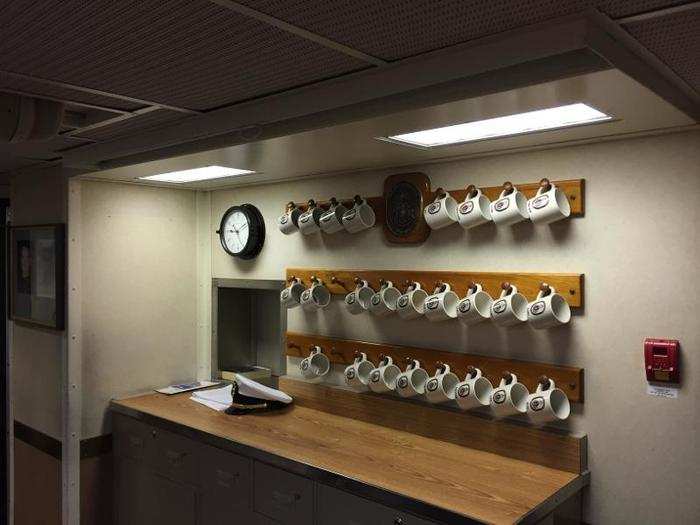 The back wall of the wardroom had rows of labeled mugs, one of them in honor of the ship