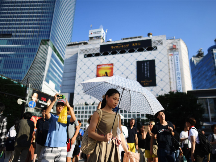 In the Shibuya district, in Tokyo, a woman protects herself from the sun with an umbrella.