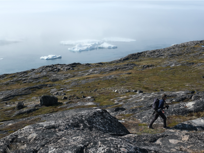 In Greenland, a visitor walks along the hillside above icebergs floating in the Ilulissat Icefjord. Summers are getting longer in Greenland and its icecap is retreating at an accelerated pace.