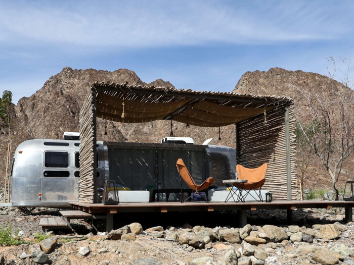 Each air conditioned, 194-square-foot trailer includes a shaded private deck, a modern bathroom, Wifi, a TV, and the option to configure the trailer to sleep a family of two adults and two children.