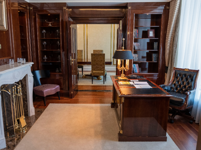 The office is outfitted with a fireplace, a stately wooden desk, and a heavy leather-and-wood desk chair.