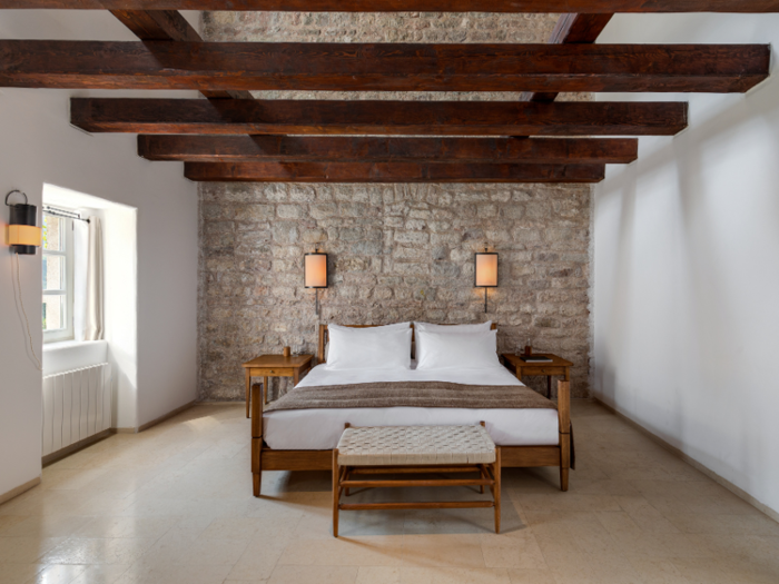 The spacious rooms in the village have a similar rustic-meets-minimalist aesthetic with wooden-beamed ceilings, exposed stone walls, and a neutral color palette.