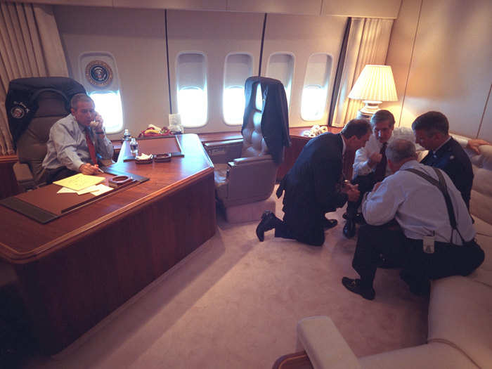 Bush talks on the telephone as senior staff huddle in his office.