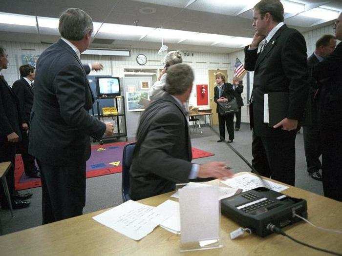 Bush watches television coverage of the attacks on the World Trade Center during a briefing in the classroom.