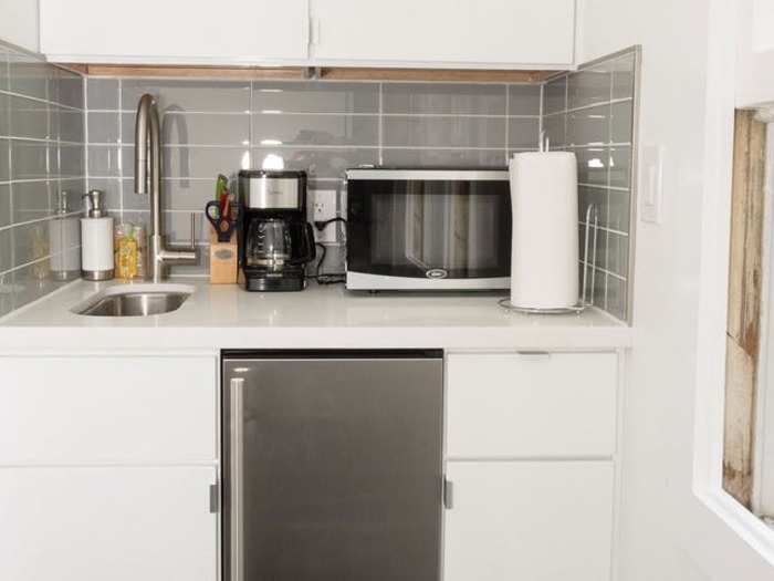 The "kitchen" consists of a mini-fridge, a minuscule sink, and cupboards, with just enough counter space for a microwave and small coffee maker.