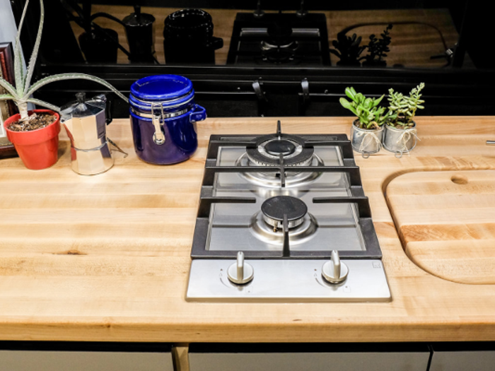 The kitchenette includes a double burner cooktop, mini-refrigerator, and a stainless steel sink with a removable cover that can be used as a cutting board.