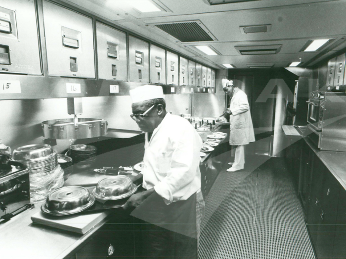 This photo, taken either late-1970s or early-1980s, shows the kitchen on a bi-level Superliner train car. The kitchen was air-conditioned and lit with fluorescent bulbs and came equipped with electric convection and microwave ovens, an electric grill, toaster, coffee maker, and a warming table.