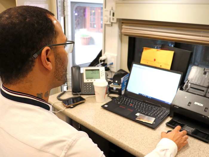 Inside the van, Nehemias Grullon, a community educator, looks at patient records and talks to incoming patients about insurance options. He collects pay stubs and general income information to help patients figure out their insurance options.