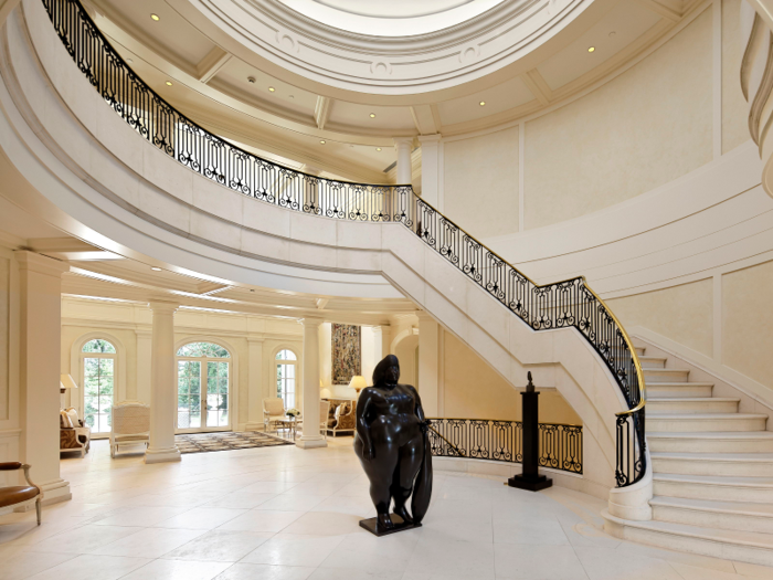 In the entry hall, an elegant staircase with wrought iron details spirals up underneath an elliptical plaster dome.