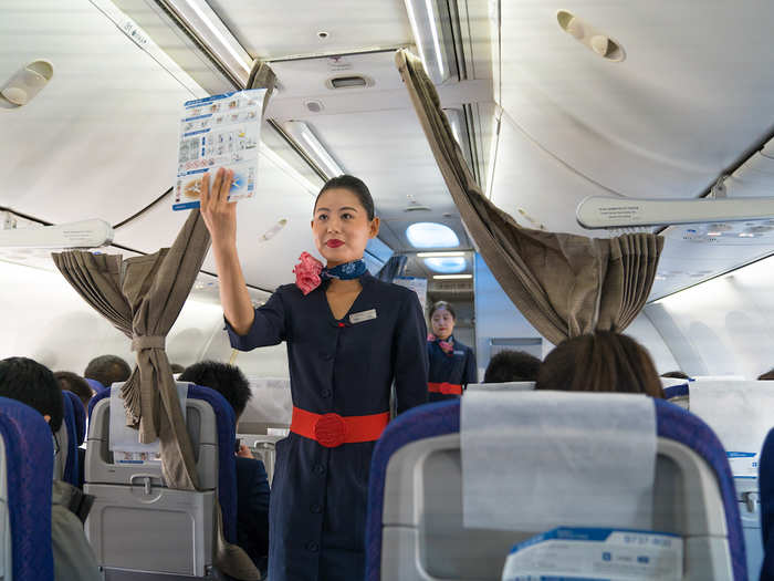 Shortly after, flight attendants — wearing a dark blue traditional Chinese dress with a red belt, and a silk scarf — started giving a safety demonstration.