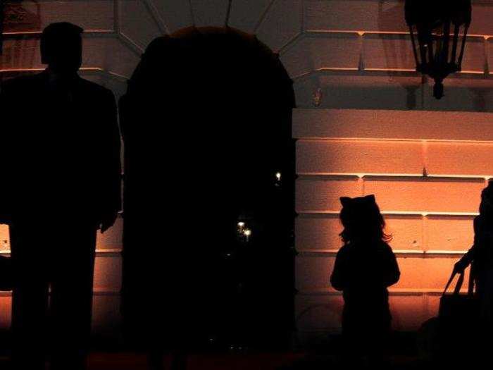 Trump and two trick-or-treaters are silhouetted by the orange light.