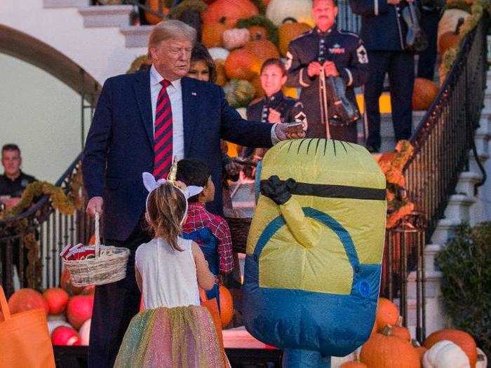 Trump is seen putting a candy bar on the head of a child dressed as a Minion from 