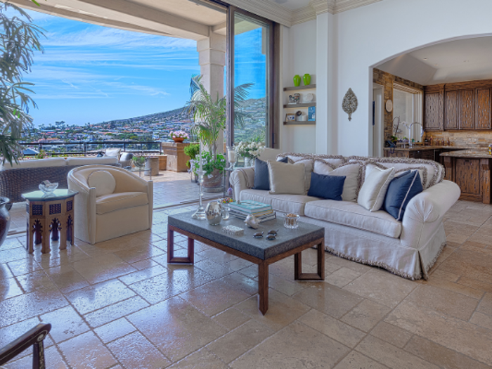 The home has multiple fireplaces, high ceilings, glass doors, and tray ceilings. The walls of glass reveal views of Laguna Beach.