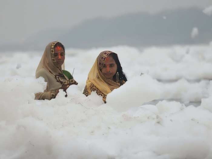 Women carry out Chatth Puja rituals in the middle of the toxic foam in the Yamuna river.