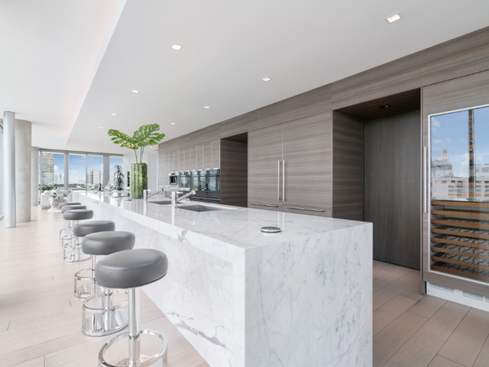 The kitchen has state-of-the-art appliances, including a wine cooler and an elongated marble island and bar.