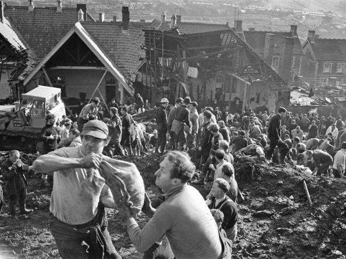 Locals and arriving emergency services worked as quickly as they could, digging through the coal-waste for survivors. They formed lines to move buckets of the sludge. In the photo below, two men are using sand bags full of mud to make a wall in case of further landslides.