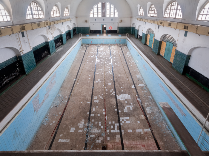 The swimming pool, completely empty of water, has remained frozen in time. You can see the lane dividers still hanging mid-air.