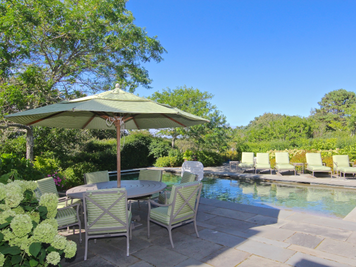 Next to the pool is an al fresco dining area shaded with trees and greenery.