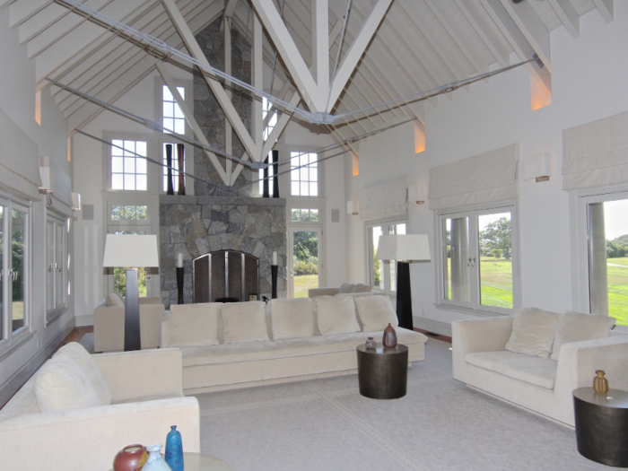 The living room features vaulted ceilings with exposed steel beams and a stone fireplace as the focal point.