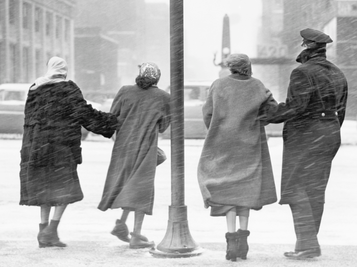 In 1945, pedestrians with linked arms waited to cross a road during a snowstorm in New York City.