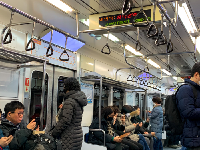 A screen on the train announces the next station, with information in Korean and English.