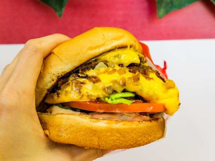 Two fresh beef patties with melted American cheese, onions, lettuce, and tomato stacked into two toasted buns are smothered in special sauce and grilled onions.