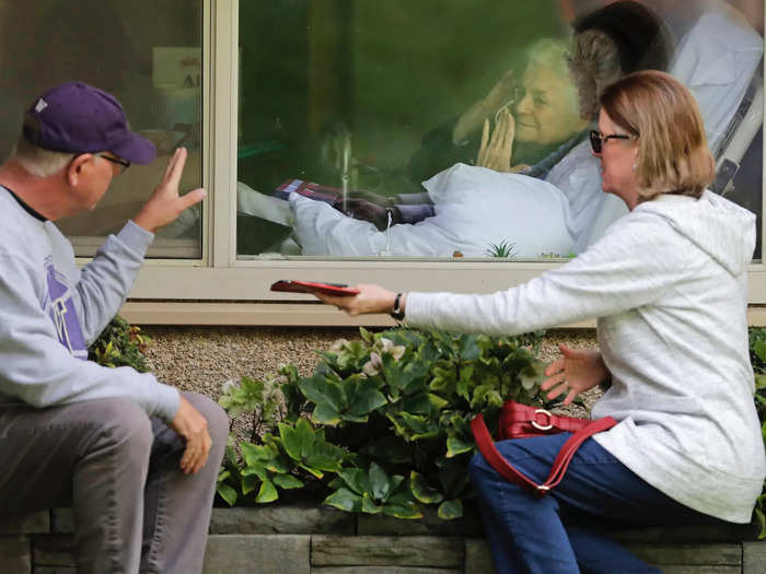 Here Judie Shape, who is behind the glass, and tested positive for the coronavirus, blows a kiss to her son-in-law, Michael Spencer.