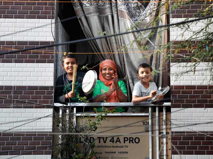 A family rings bells, hits pots and pans, and cheers together from a balcony in New Delhi, India.