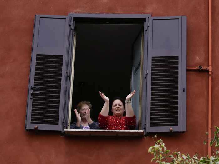 Women lean out of their home in Rome, Italy, to cheer.