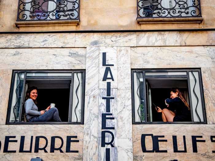 Two women are seen having a socially distant cup of coffee from their apartment windows in France.