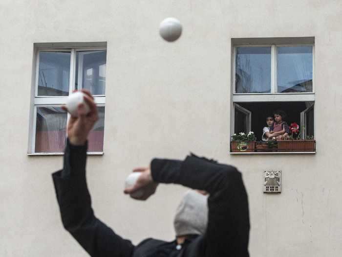 In Prague, children look out of their windows to watch jugglers and other members of a contemporary circus company perform on a courtyard rooftop.