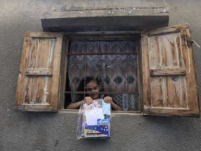 In Palestine, a girl shows off a package of reading material and art supplies that volunteers distributed for children under isolation.